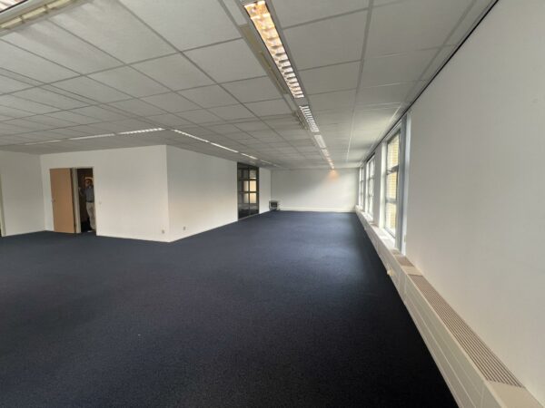 Lege kantoorruimte aan de Rivium 2e Straat met donker tapijt, systeemplafond en grote ramen aan de rechterkant.